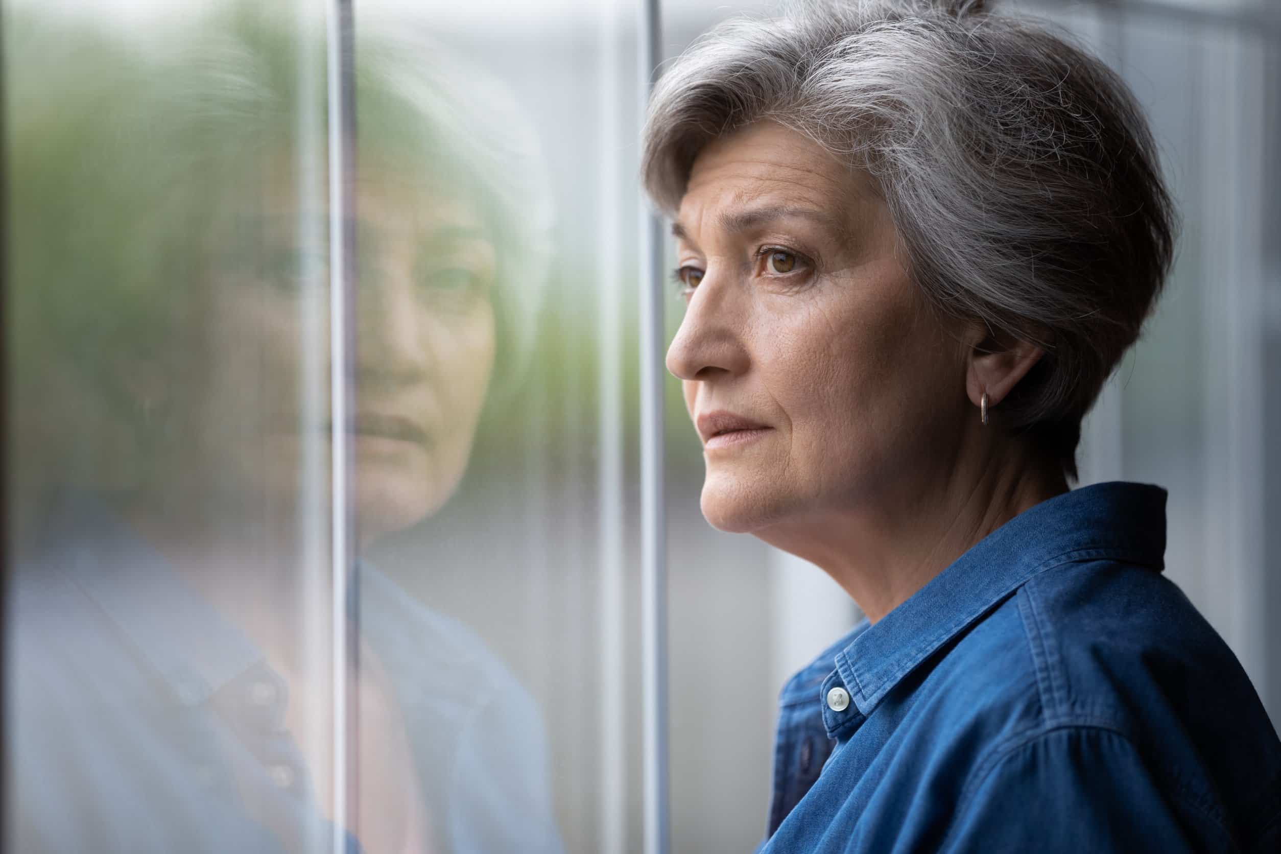 Close up thoughtful mature woman looking out window at home