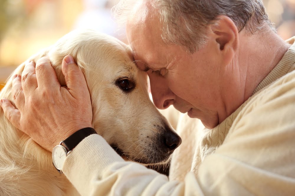 Man leaning his head against his dog's head