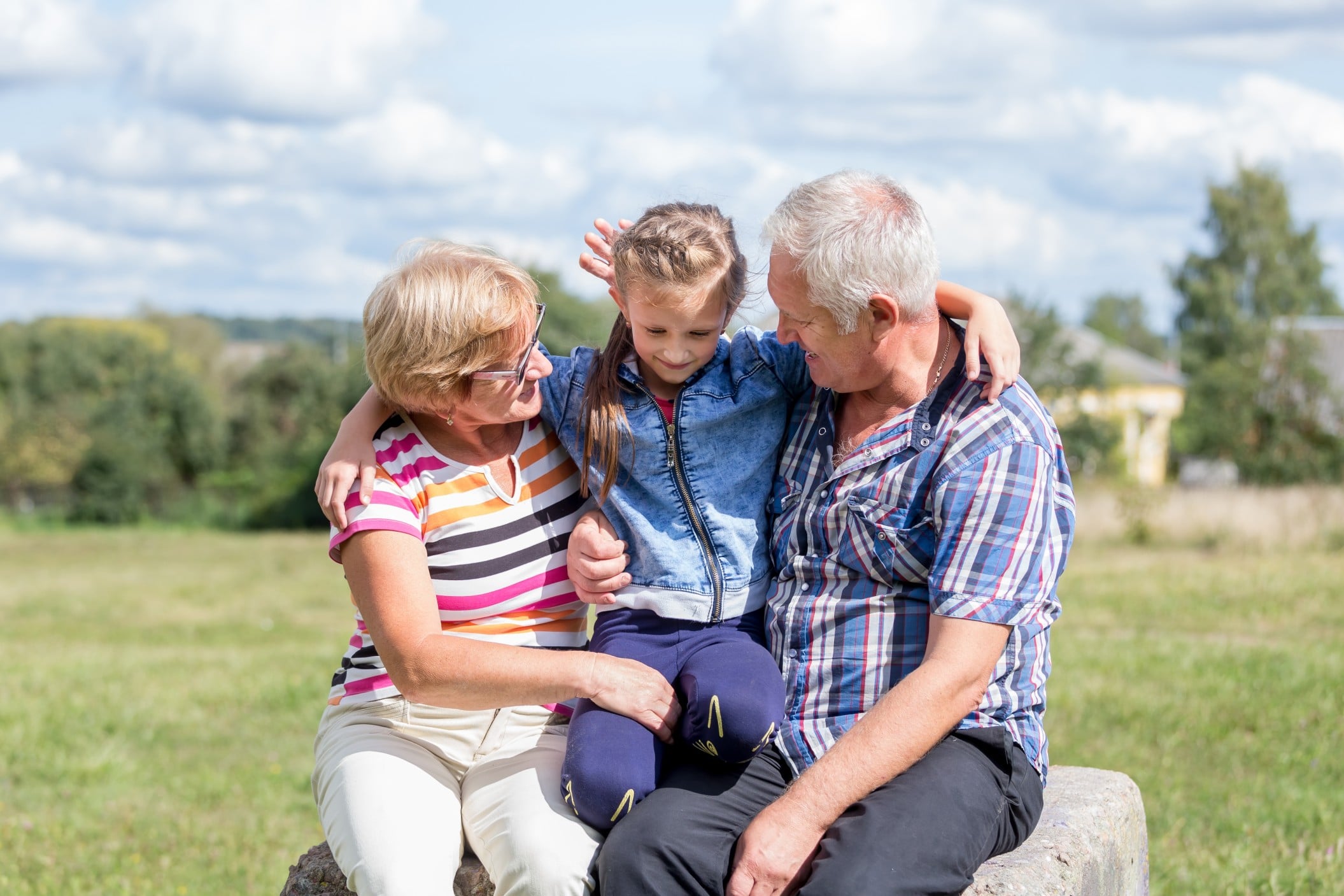 Grandparents with Granddaughter in a grassy field on a sunny day
