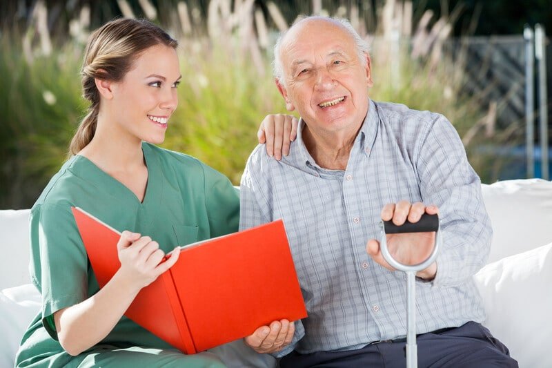 Portrait of happy senior man sitting by female nurse holding book