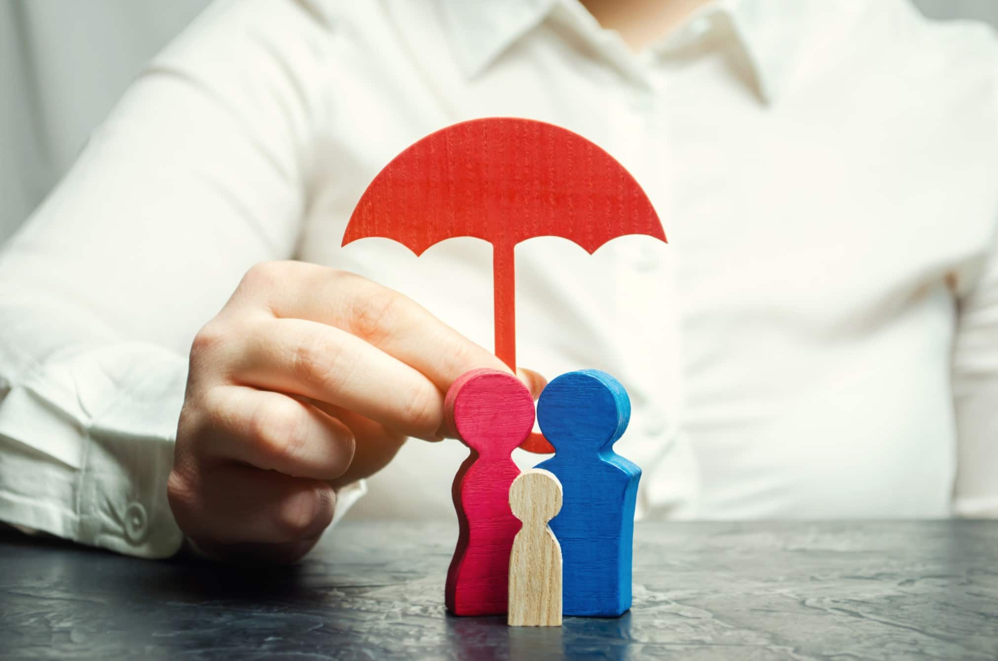 Miniature wooden figures of people in the form of a family covered by an umbrella cutout