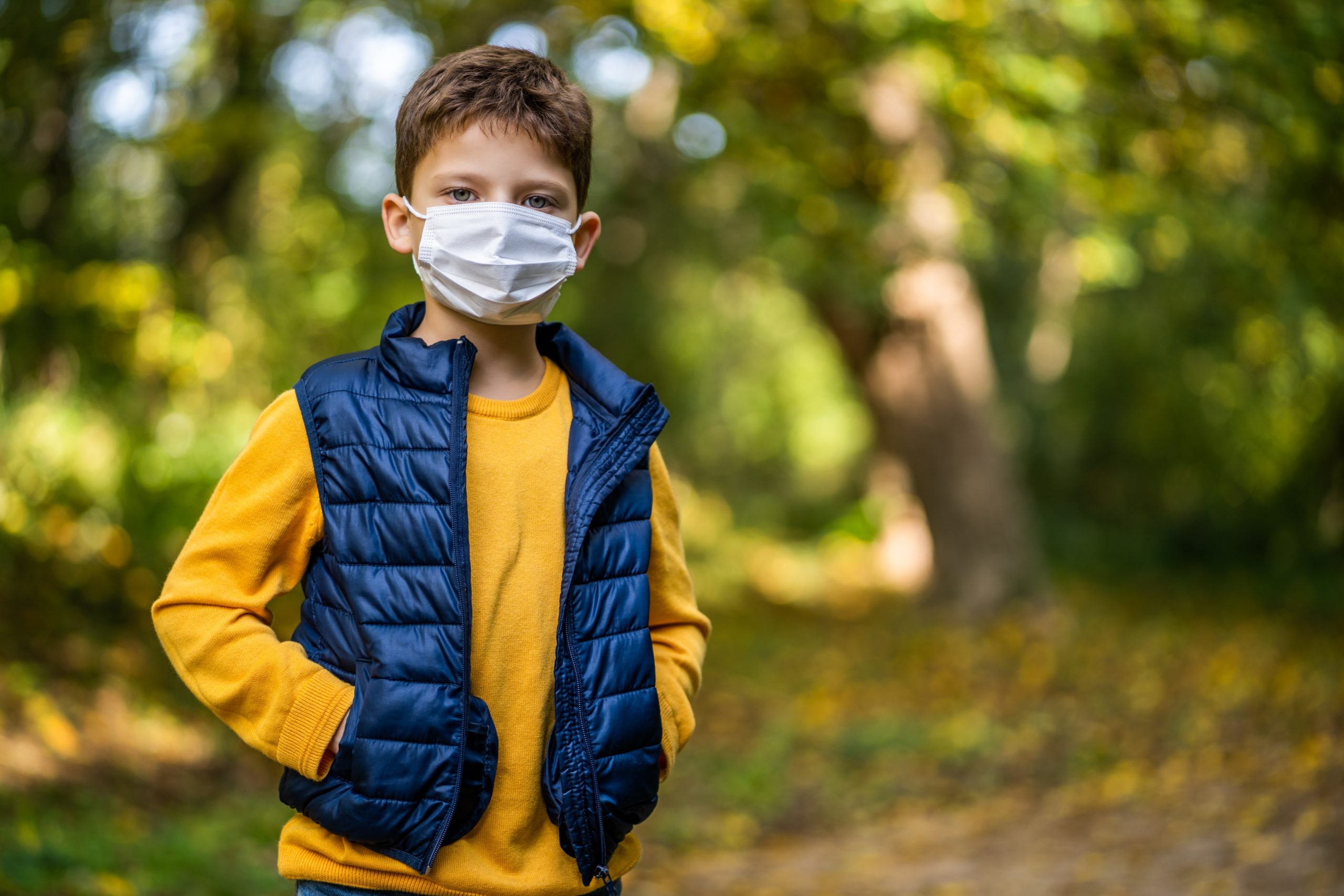 Boy wearing yellow shirt, navy blue vest, and face mask