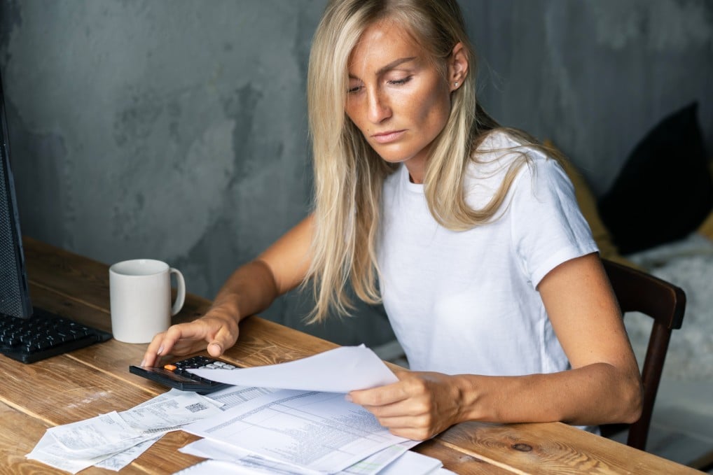 Woman in a white shirt sitting at a desk holding a calculator and reviewing a stack of bills