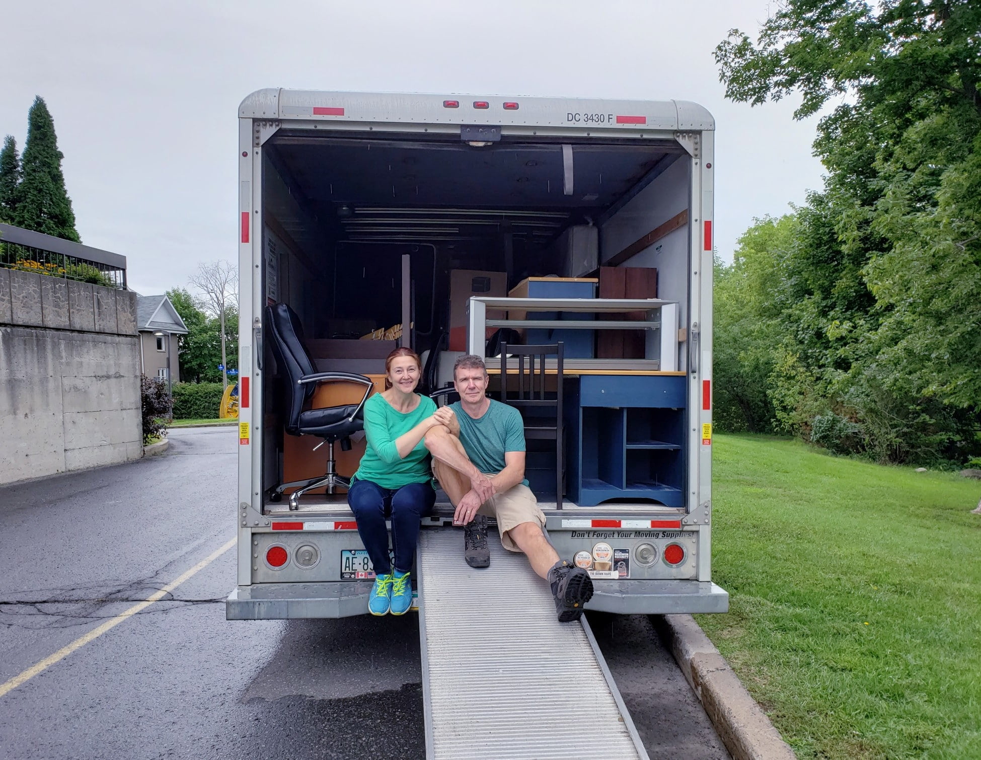 Couple is ready to move into new place--sitting on a moving truck filled with furniture