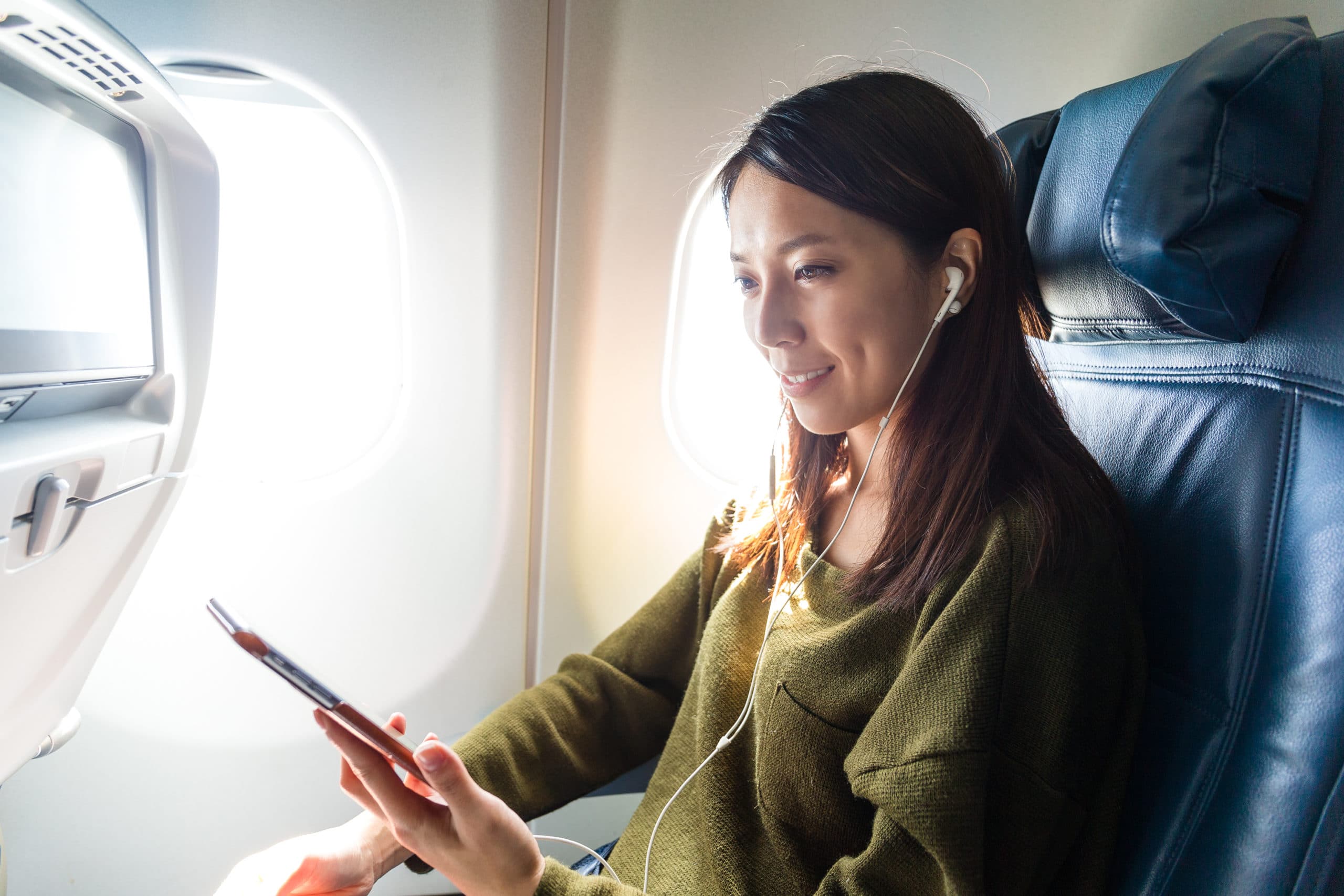 Woman listens to music on a mobile phone while sitting in an airplane seat